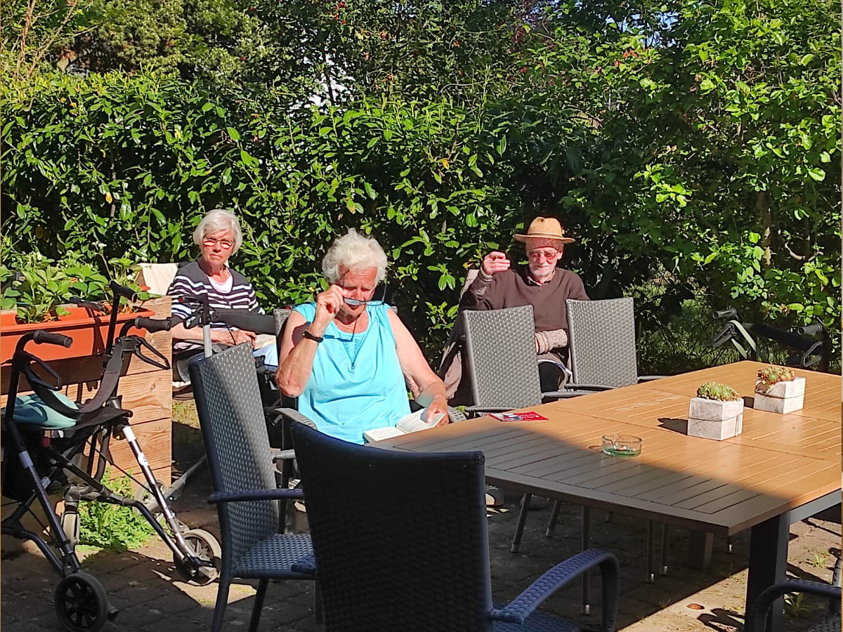 Drei Bewohner sitzen in der Sonne im Garten und Lesen.