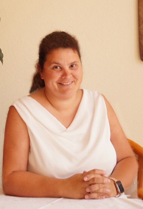 Frau Katrin Volgmann-Röchert sitzt an einem Tisch und lächelt freundlich.