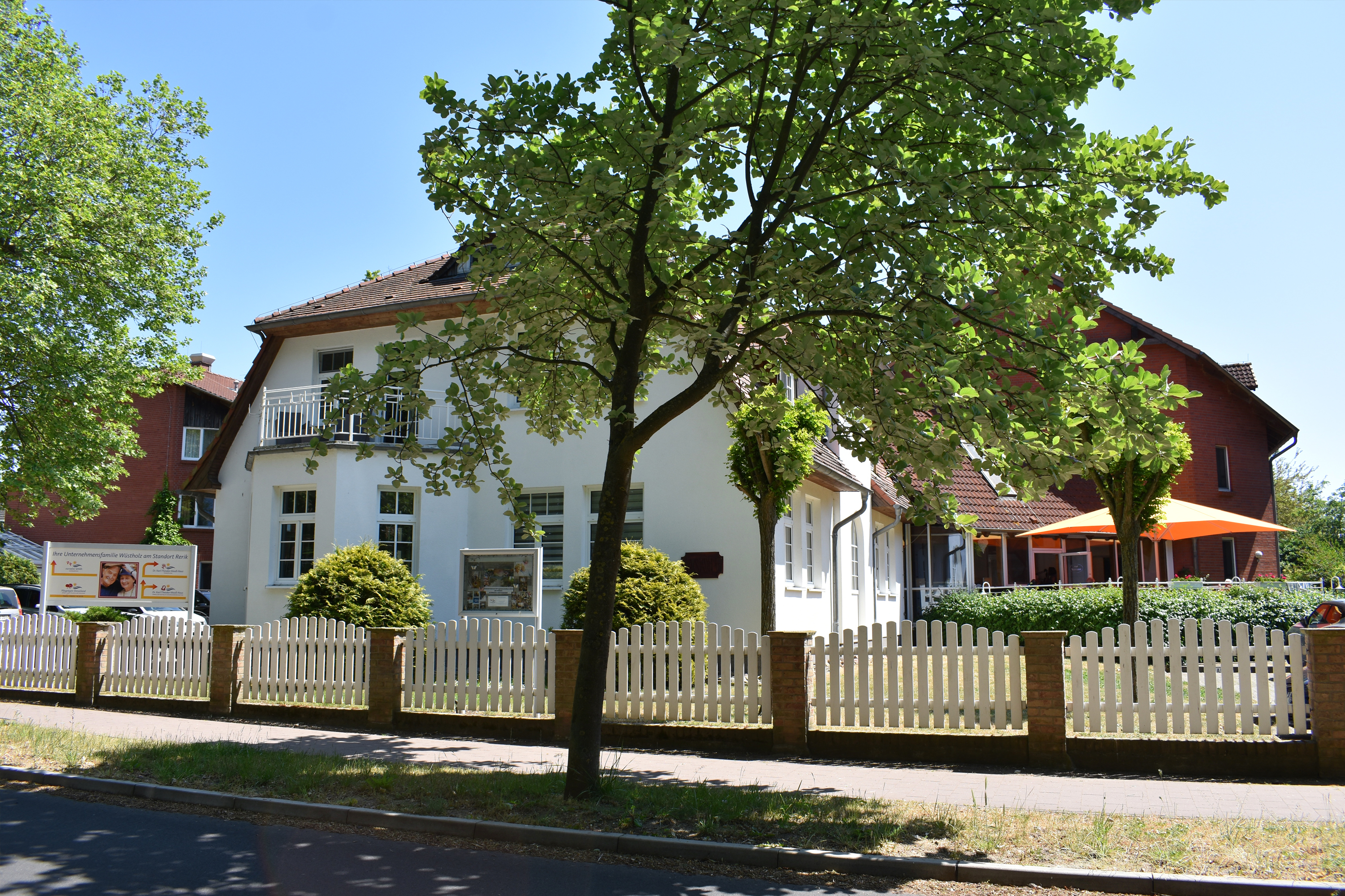 Straßenansicht des Hauses mit grünen Bäumen und blauem Himmel..