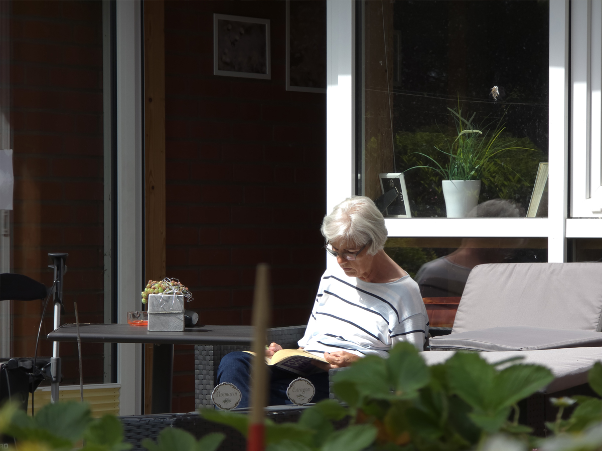 Eine Seniorin sitzt in der Sonne in einem unserer Außenbereiche und ließt entspannt ein gutes Buch.