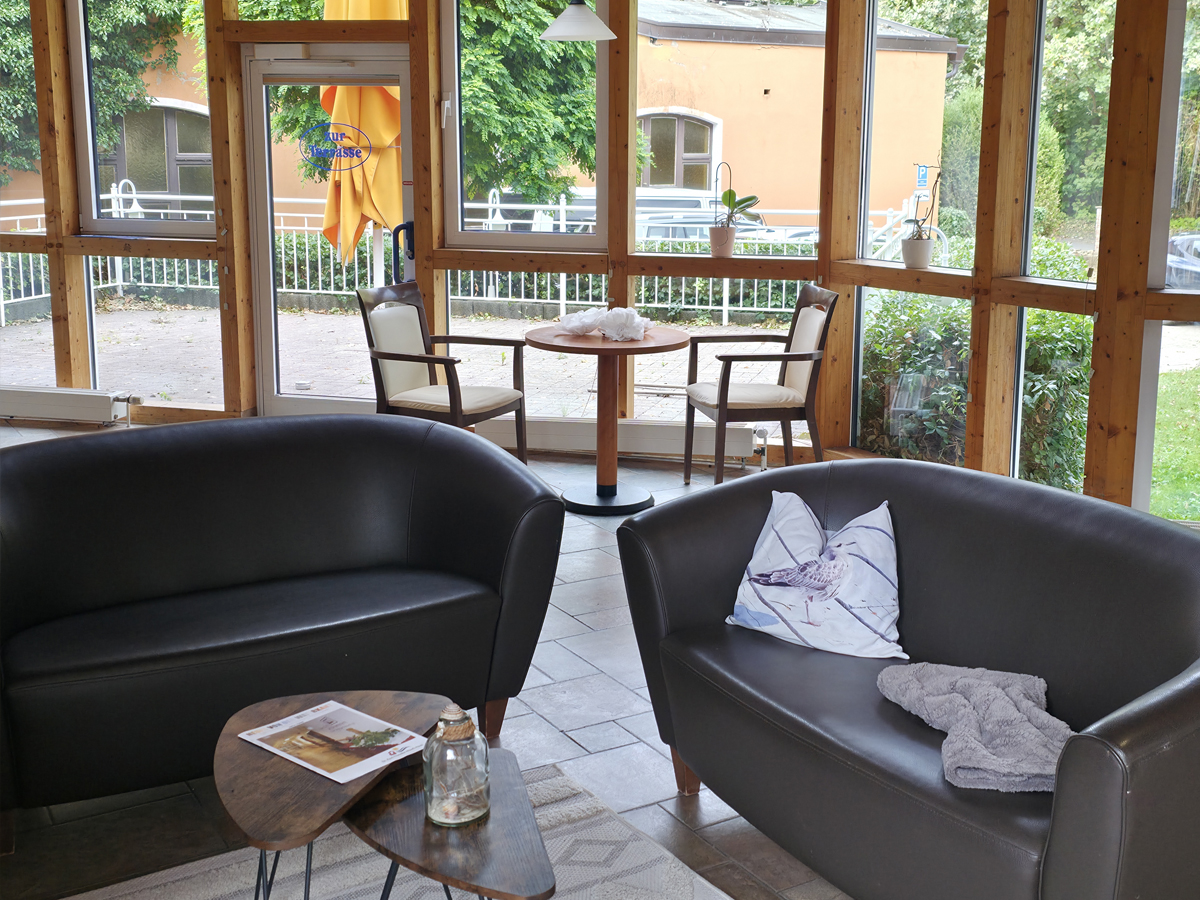 Der Gemeinschaftsbereich im Erdgeschoss. Die Sitzmöbel stehen vor einer großen Glasfront, die zur großen Terrasse führt.
