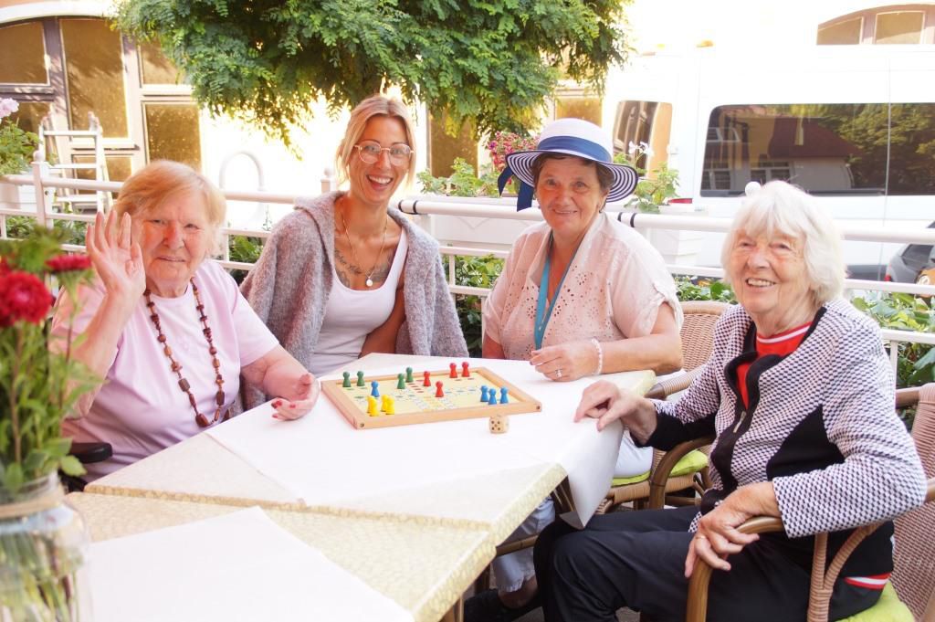 Drei Seniorinnen sitzen mit einer Betreuerin auf unserer Terrasse und spielen Brettspiele